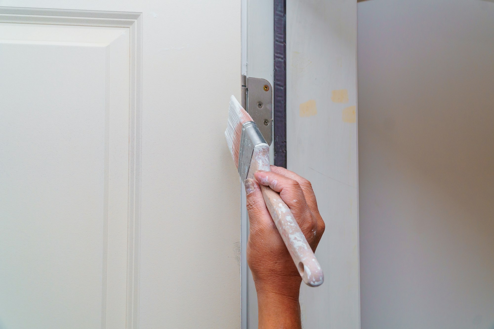Contractor painting a wooden door white in a new house